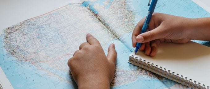 close up of kid point at a US map with a notepad and pencil