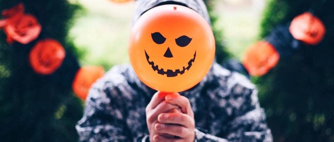 Man holding a fake pumpkin on a stick in front of his face with more pumpkins hanging in the background