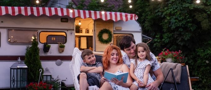 family of four sitting in front of cute RV reading a book
